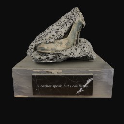 Concrete finished high heeled shoe wrapped in lace doily on top of a grey plinth